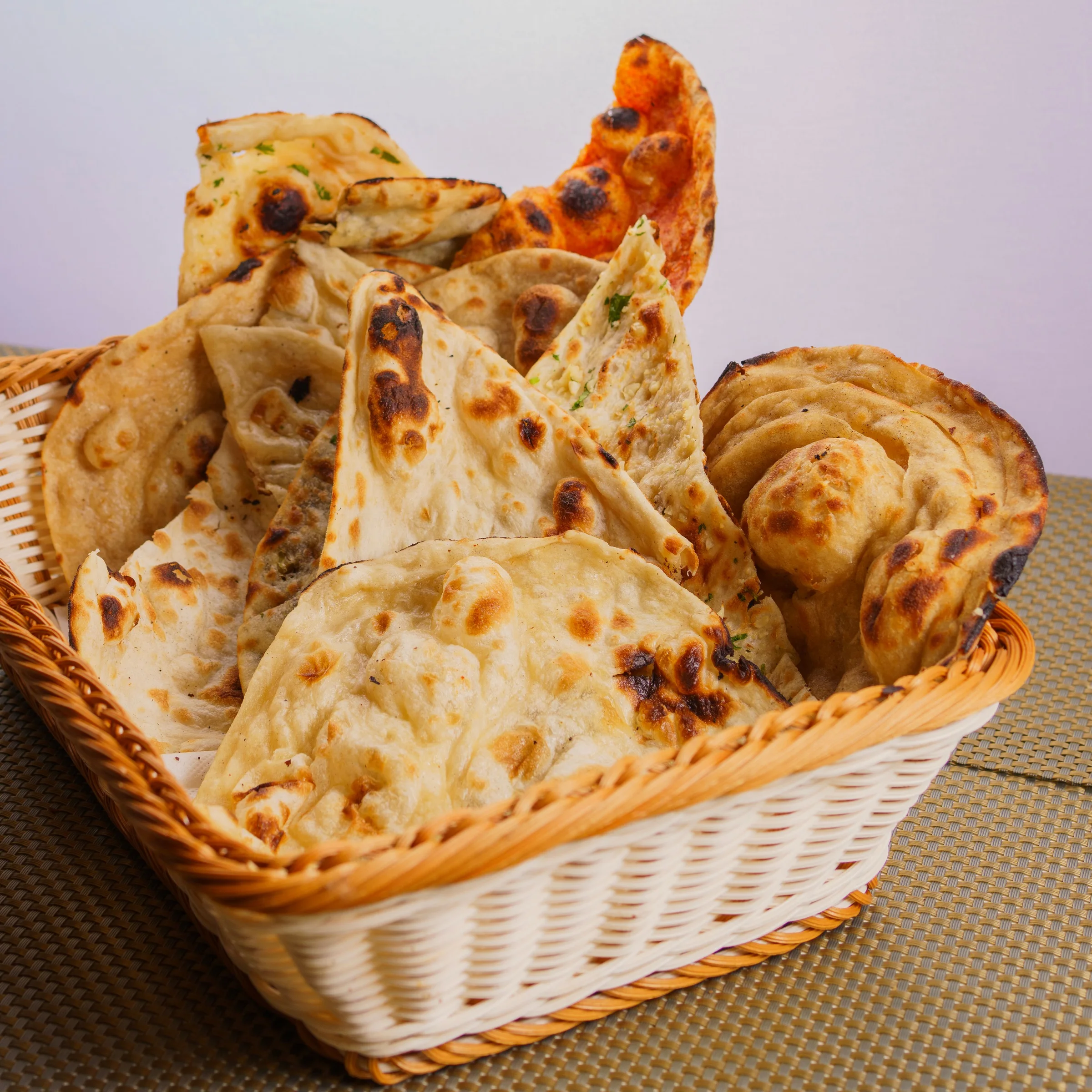 Basket of assorted naan and paratha breads with char spots