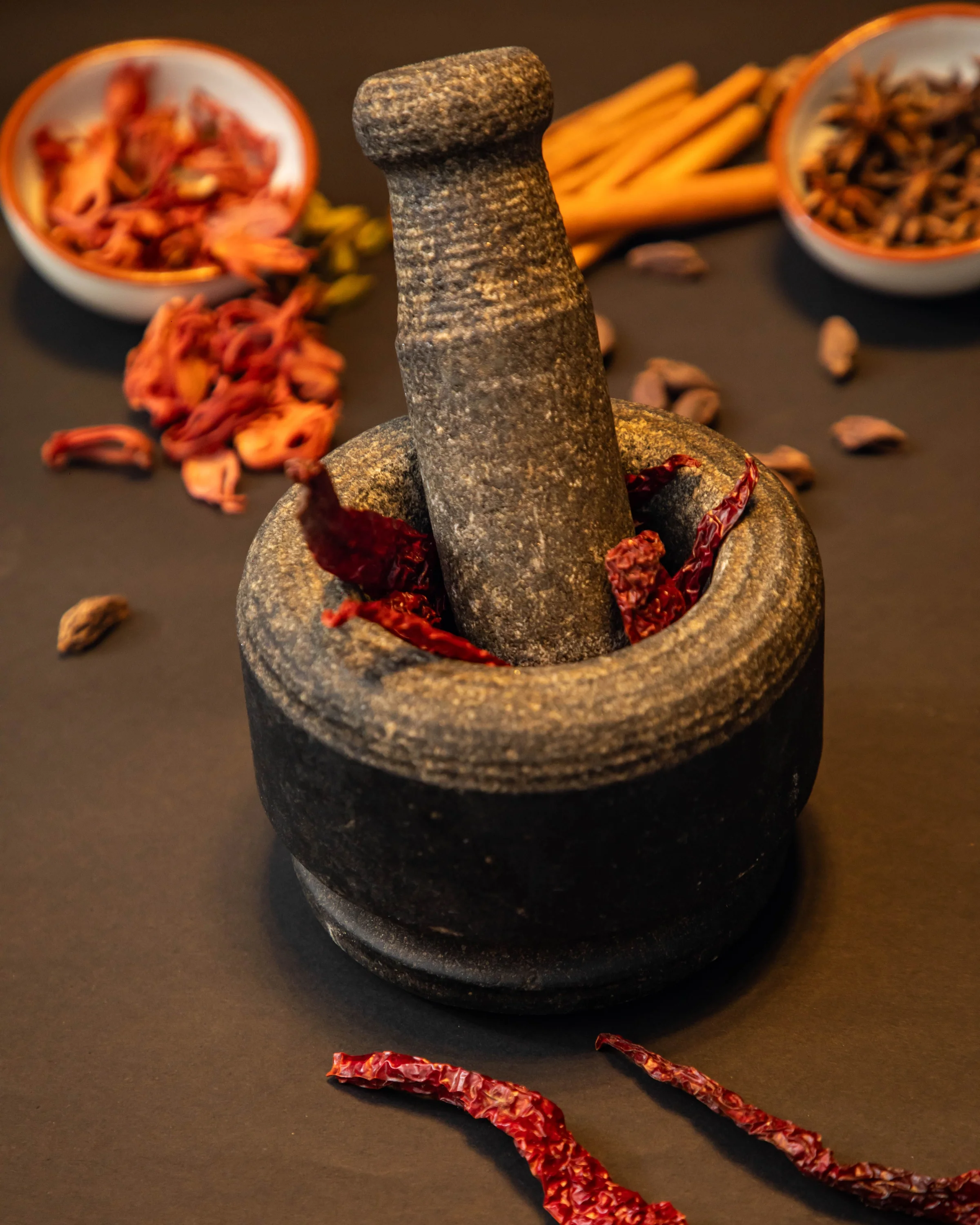 Mortar and pestle with whole Indian spices — cinnamon, star anise, dried chiles, and cardamom